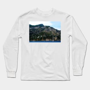 View in Amalfi coast at a huge mountain with rocky parts, greenery and buildings with a white boat underneath Long Sleeve T-Shirt